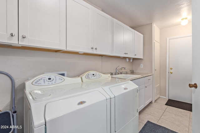 clothes washing area featuring light tile patterned flooring, sink, washing machine and clothes dryer, and cabinets