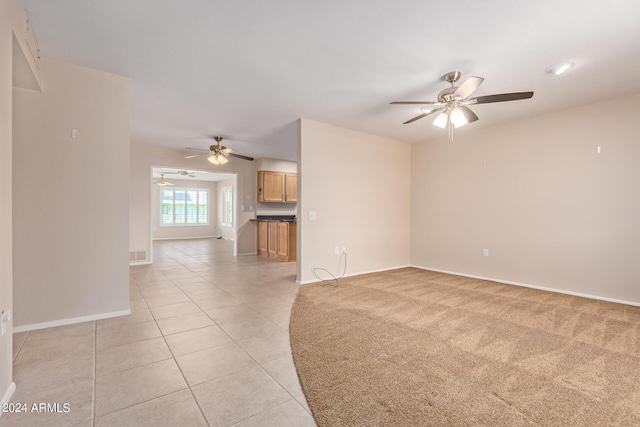 unfurnished living room with light tile patterned floors, light carpet, visible vents, a ceiling fan, and baseboards