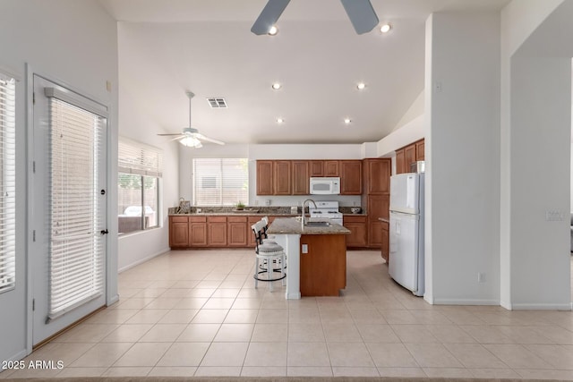 7231 W Lone Cactus Dr, Glendale, AZ 85308 - kitchen featuring a ceiling fan, white appliances, brown cabinetry, a breakfast bar area, and an island with sink