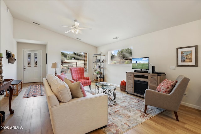 living room featuring a fireplace, lofted ceiling, visible vents, a ceiling fan, and light wood-type flooring