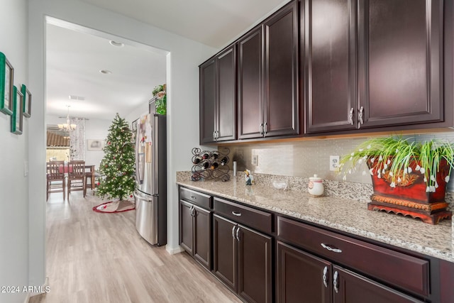 kitchen featuring decorative backsplash, stainless steel fridge, light wood-type flooring, dark brown cabinets, and a notable chandelier