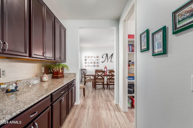 kitchen with dark brown cabinetry, decorative backsplash, light stone counters, and light wood-type flooring