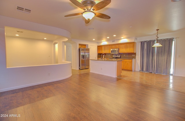 kitchen with a kitchen island with sink, stainless steel appliances, backsplash, sink, and light hardwood / wood-style floors