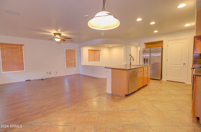 kitchen featuring an island with sink, stainless steel appliances, sink, light hardwood / wood-style floors, and decorative light fixtures