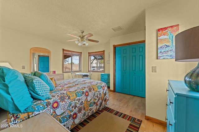 bedroom with arched walkways, visible vents, a ceiling fan, a textured ceiling, and light wood-type flooring