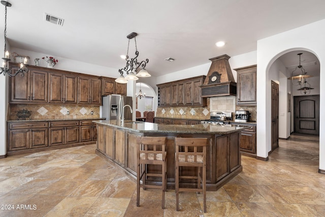 kitchen featuring a center island with sink, pendant lighting, custom range hood, and stainless steel fridge