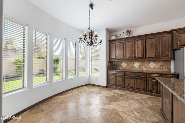 kitchen featuring hanging light fixtures, dark brown cabinetry, dark stone counters, decorative backsplash, and stainless steel fridge