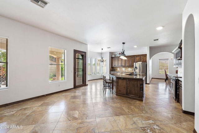 kitchen with appliances with stainless steel finishes, decorative light fixtures, a wealth of natural light, a kitchen island, and a kitchen bar