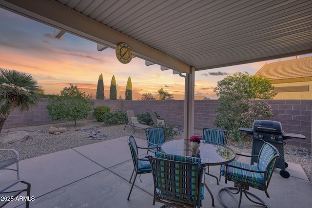 patio terrace at dusk with outdoor dining space, a fenced backyard, and area for grilling