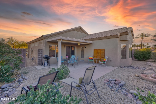 rear view of house featuring a patio area, fence, a tile roof, and stucco siding