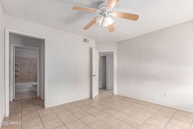 unfurnished bedroom with a textured ceiling, light tile patterned floors, ensuite bath, and a ceiling fan