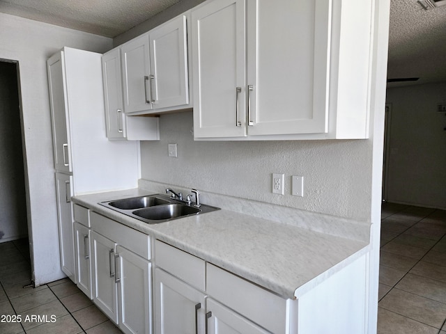 kitchen with a sink, a textured ceiling, light tile patterned floors, and white cabinets