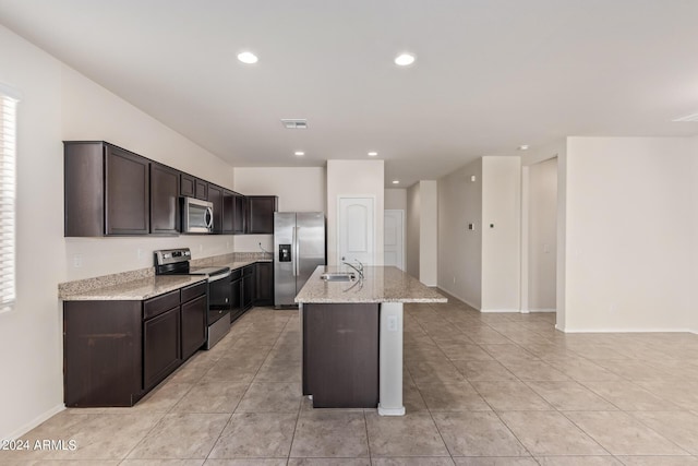 kitchen with light stone counters, recessed lighting, stainless steel appliances, a sink, and a center island with sink