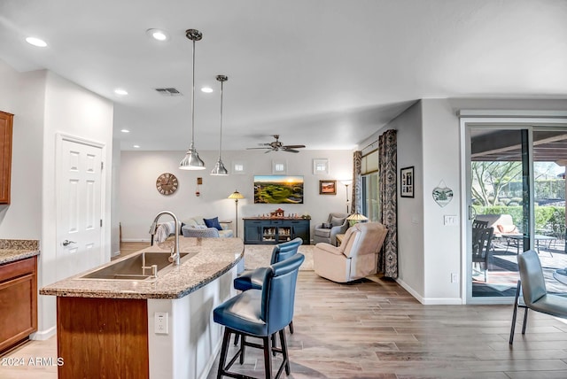 kitchen featuring a kitchen island with sink, sink, light hardwood / wood-style flooring, ceiling fan, and decorative light fixtures