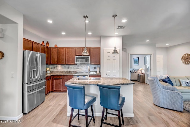 kitchen featuring light hardwood / wood-style flooring, an island with sink, pendant lighting, and appliances with stainless steel finishes