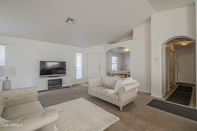 living area with arched walkways, carpet floors, visible vents, baseboards, and vaulted ceiling