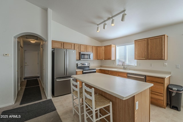 kitchen with arched walkways, a center island, vaulted ceiling, stainless steel appliances, and a sink