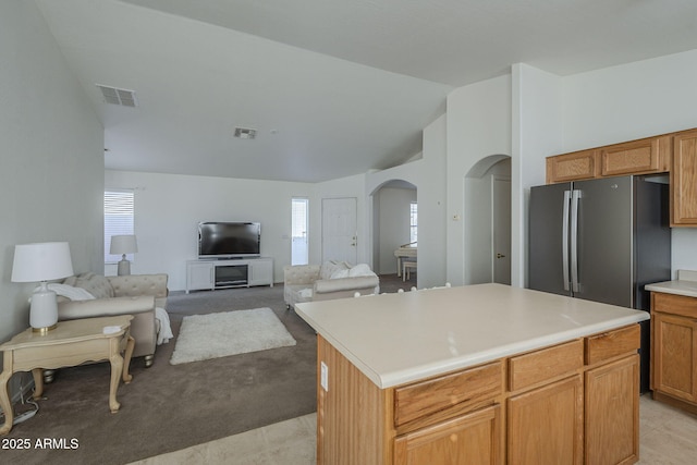 kitchen with lofted ceiling, visible vents, arched walkways, and freestanding refrigerator