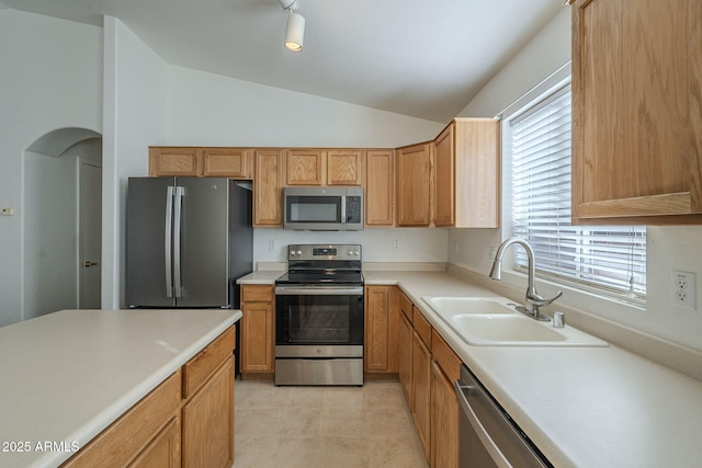 kitchen with arched walkways, appliances with stainless steel finishes, vaulted ceiling, light countertops, and a sink