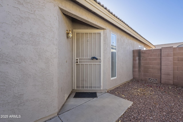 doorway to property with a tile roof, fence, and stucco siding