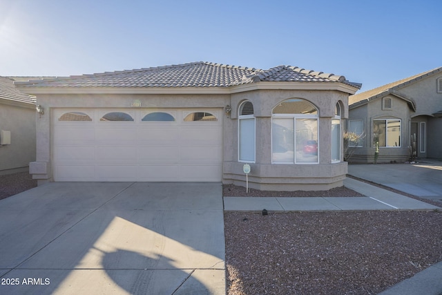 view of front facade with an attached garage, a tile roof, concrete driveway, and stucco siding