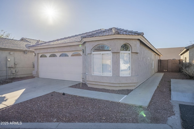 view of front facade with a tile roof, stucco siding, an attached garage, fence, and driveway