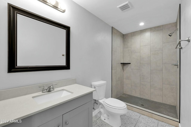 bathroom with tiled shower, tile patterned flooring, vanity, and toilet