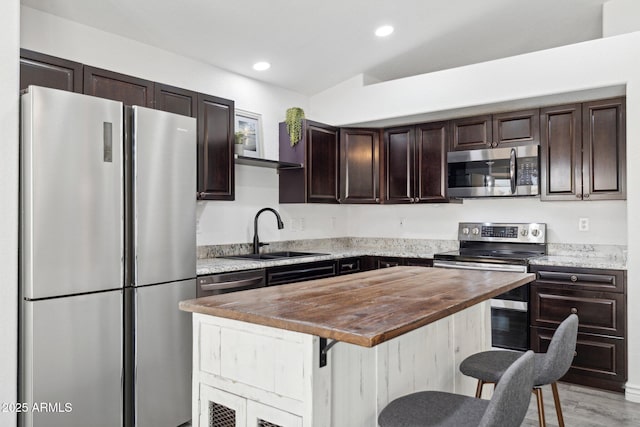 kitchen with dark brown cabinets, a breakfast bar area, recessed lighting, a sink, and appliances with stainless steel finishes