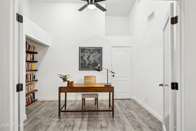 office space featuring visible vents, baseboards, a high ceiling, a ceiling fan, and light wood finished floors