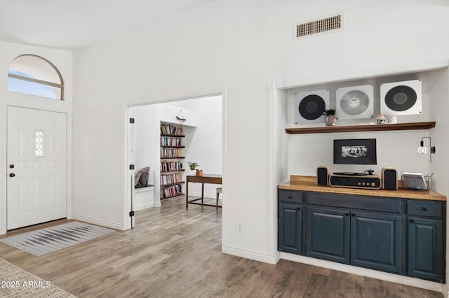 foyer entrance with baseboards, visible vents, wood finished floors, and a high ceiling