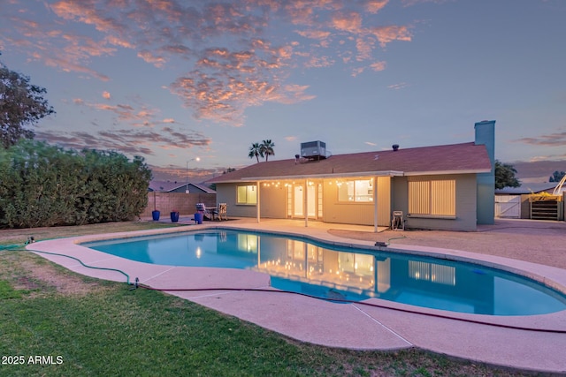 pool at dusk featuring a fenced in pool, a yard, a patio area, and fence