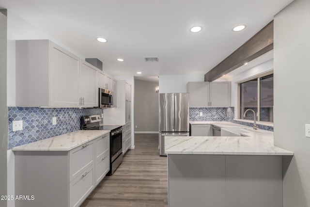 kitchen featuring light stone counters, visible vents, a peninsula, a sink, and appliances with stainless steel finishes