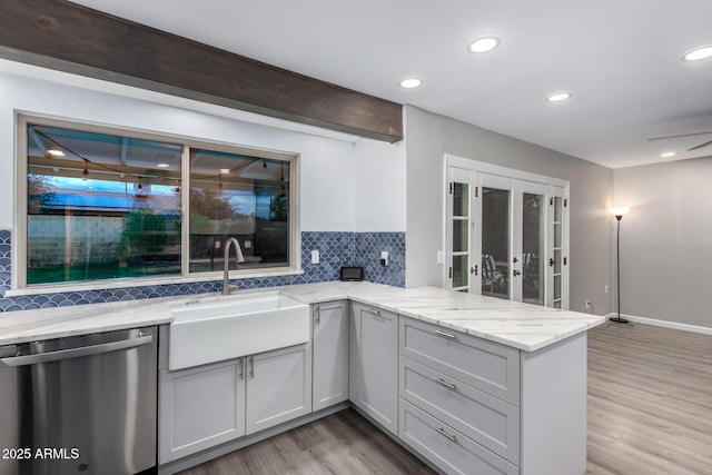 kitchen featuring a sink, backsplash, a peninsula, light stone countertops, and dishwasher