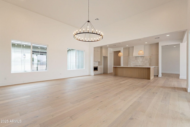 6832 N 178th Ln, Waddell, AZ 85355 - unfurnished living room with baseboards, light wood finished floors, a sink, a towering ceiling, and a notable chandelier