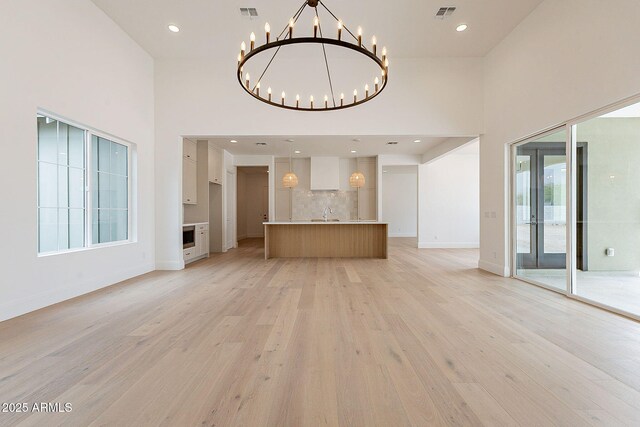 6832 N 178th Ln, Waddell, AZ 85355 - unfurnished living room featuring a notable chandelier, a high ceiling, light wood-type flooring, and visible vents