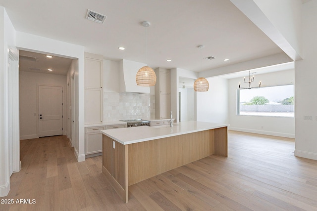 6832 N 178th Ln, Waddell, AZ 85355 - kitchen featuring visible vents, light wood finished floors, a large island with sink, decorative backsplash, and light countertops