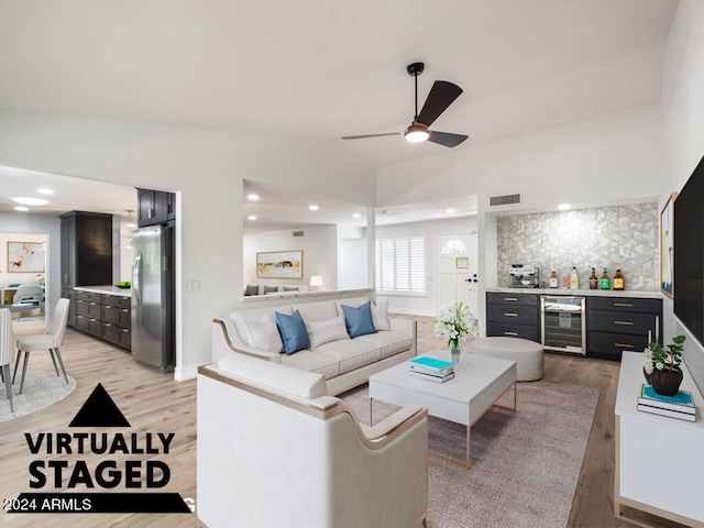 living room featuring ceiling fan, beverage cooler, bar, light wood-type flooring, and vaulted ceiling