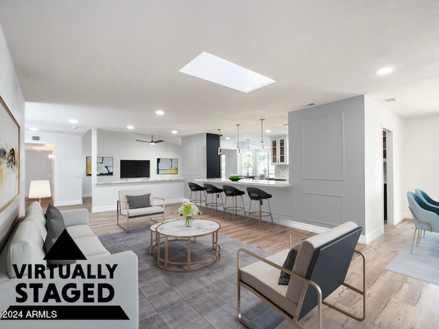 living room featuring hardwood / wood-style flooring, ceiling fan, and a skylight