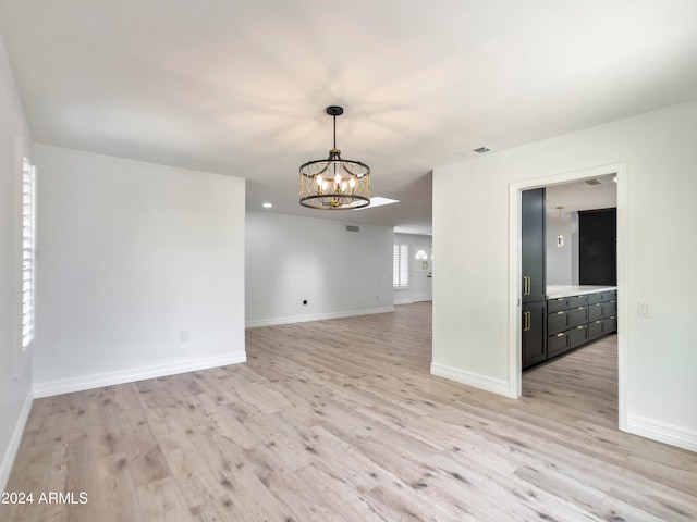 empty room with light hardwood / wood-style flooring and an inviting chandelier