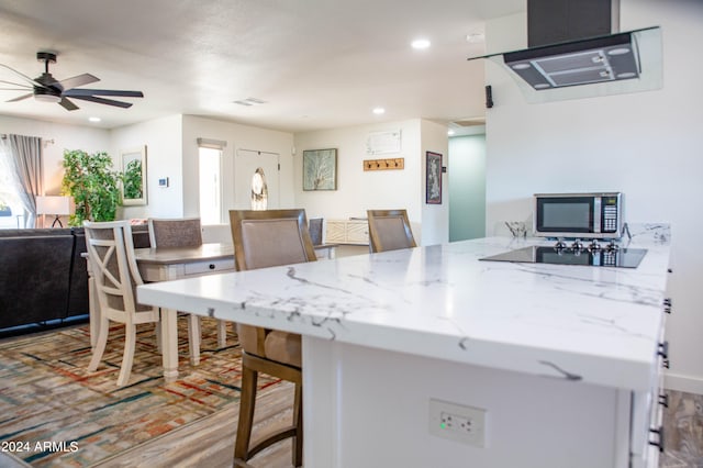 kitchen featuring ceiling fan, kitchen peninsula, light hardwood / wood-style flooring, a breakfast bar, and light stone countertops