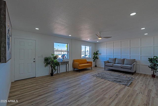 living room with a textured ceiling, ceiling fan, and light hardwood / wood-style flooring