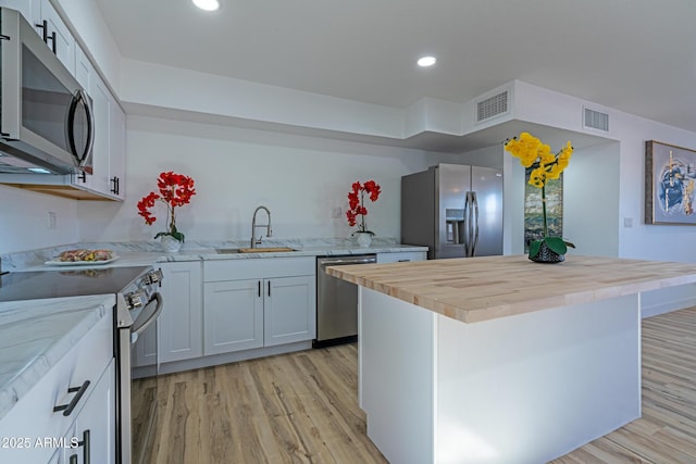 kitchen featuring appliances with stainless steel finishes, a center island, white cabinetry, sink, and light hardwood / wood-style flooring