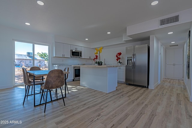 kitchen featuring appliances with stainless steel finishes, light wood-type flooring, a kitchen island, white cabinets, and a breakfast bar