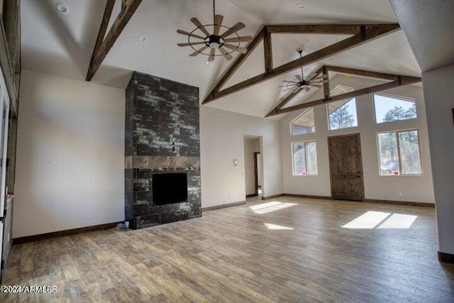 unfurnished living room featuring ceiling fan, high vaulted ceiling, wood finished floors, beam ceiling, and a tiled fireplace