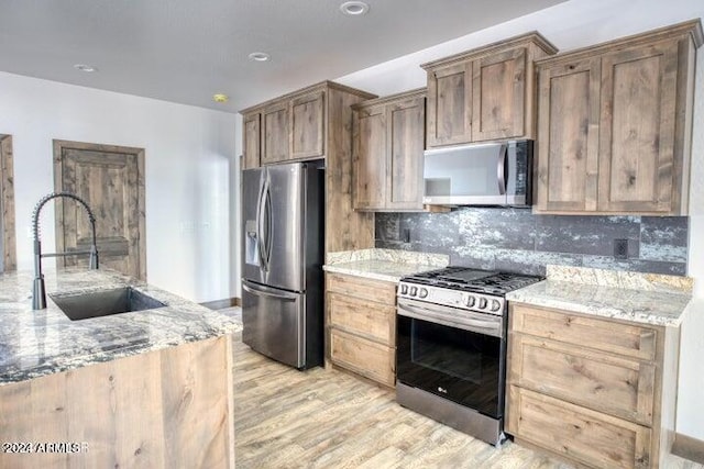 kitchen with light stone counters, stainless steel appliances, decorative backsplash, light wood-style floors, and a sink