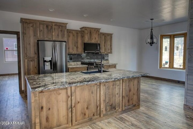 kitchen with stainless steel refrigerator with ice dispenser, light stone countertops, sink, and pendant lighting