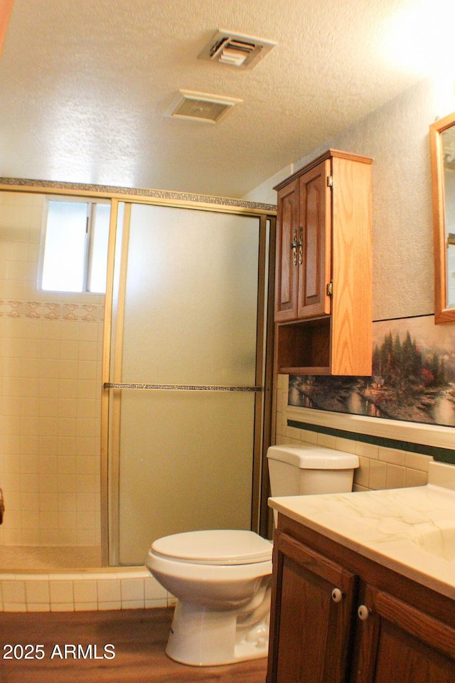 bathroom featuring a shower with shower door, backsplash, vanity, toilet, and a textured ceiling