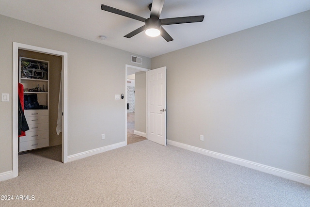 unfurnished bedroom with ceiling fan, a spacious closet, light carpet, and a closet