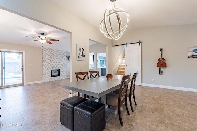 dining area featuring a tiled fireplace, a barn door, ceiling fan with notable chandelier, and lofted ceiling