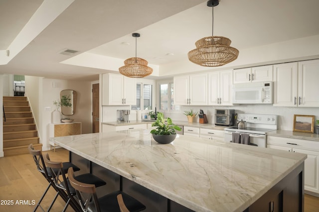 kitchen with a center island, pendant lighting, white cabinets, and white appliances